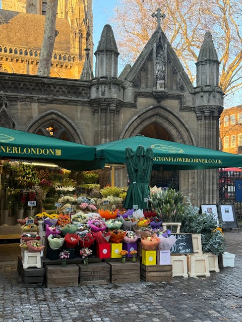 An outdoor flower stall set against the historic architecture of a church or cathedral with pointed arches and stone detailing, featuring a variety of fresh floral arrangements in vibrant colours such